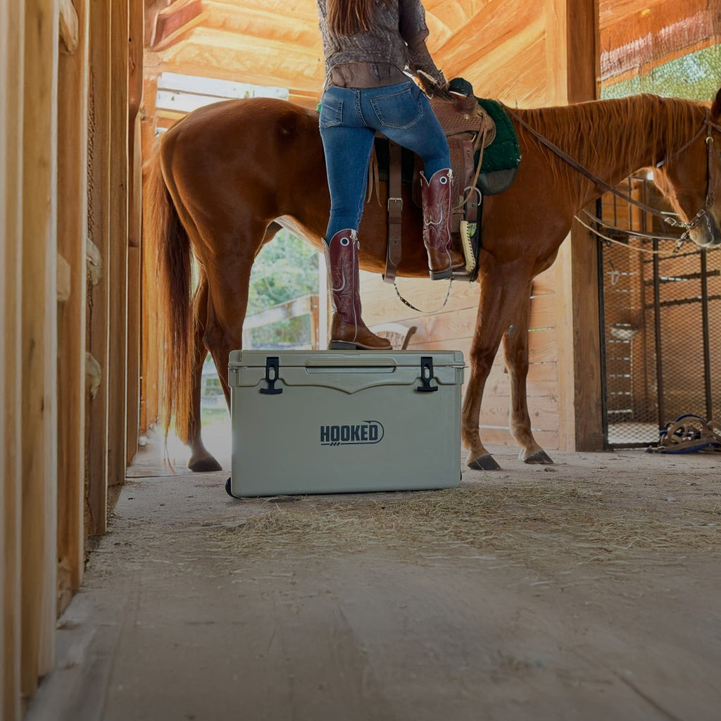 Person stepping onto a tan Hooked cooler to mount a horse.